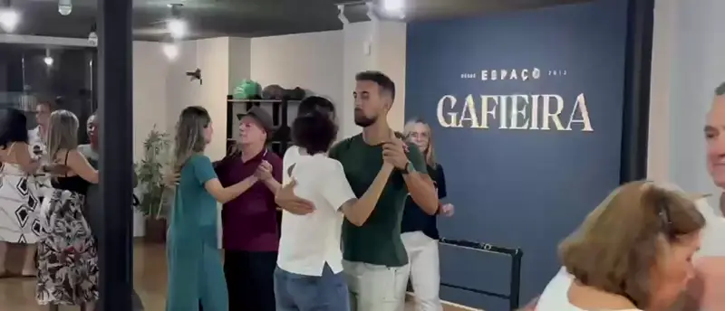 Casais dançando numa aula do Espaço Gafieira, com a parede azul da escola ao fundo