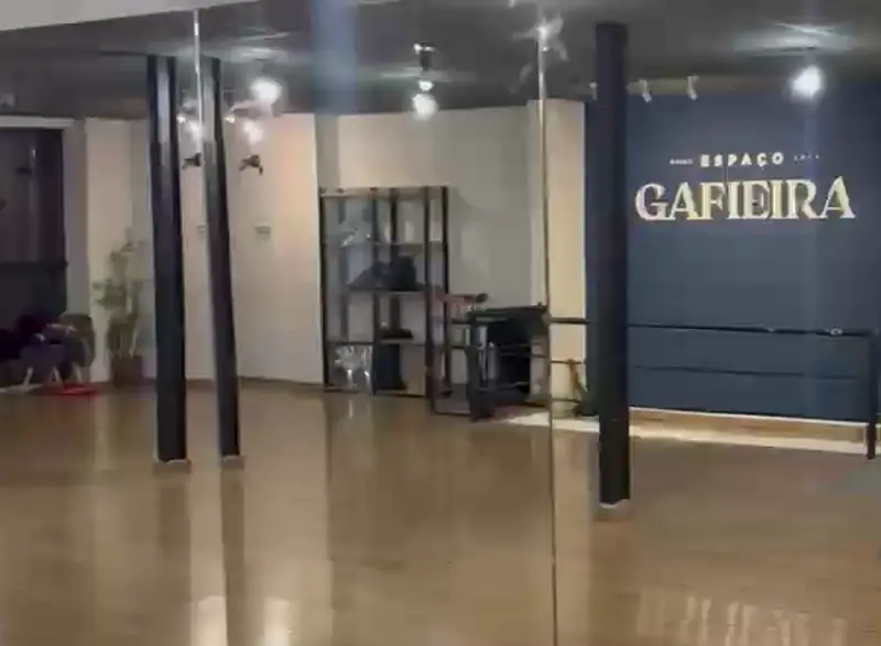Salão do Espaço Gafieira vazio, com piso de madeira e a parede azul com o letreiro